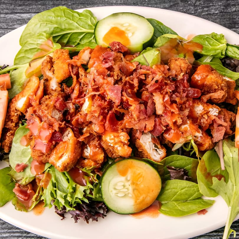 Crispy chicken salad with bacon bits, mixed greens, cucumber slices, and orange dressing.
