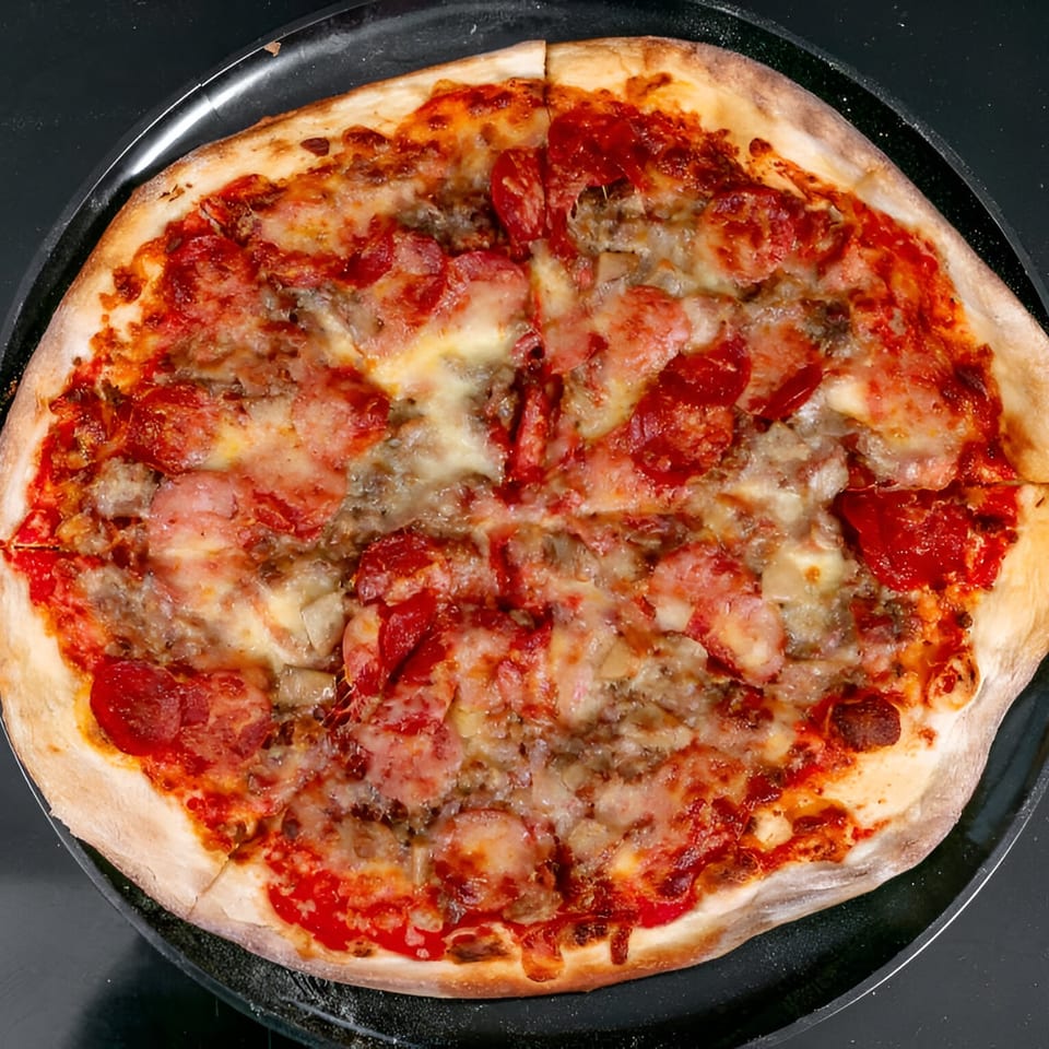 A whole Bruno's Pizza with pepperoni, sausage, and cheese on a black pan.