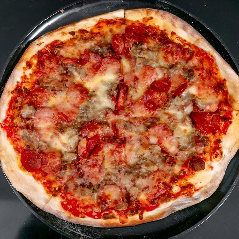 A whole Bruno's Pizza with pepperoni, sausage, and cheese on a black pan.