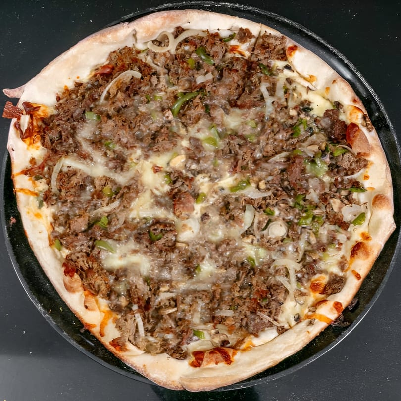 Bruno's Pizza with steak, onions, green peppers, and melted cheese on a dark pan.