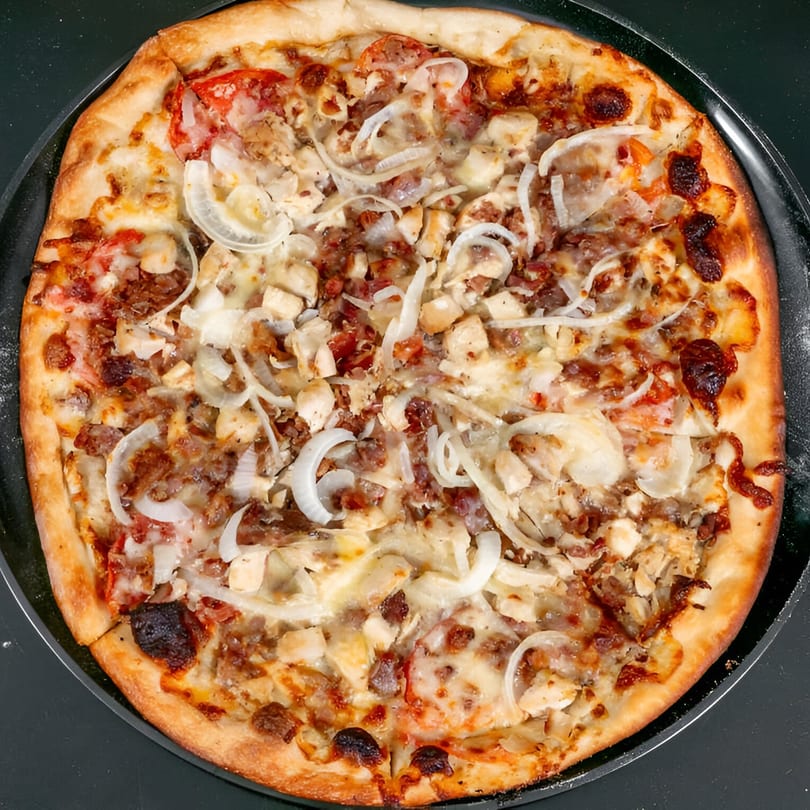 Bruno's Pizza with chicken, bacon, onions, and tomatoes on a dark pan.