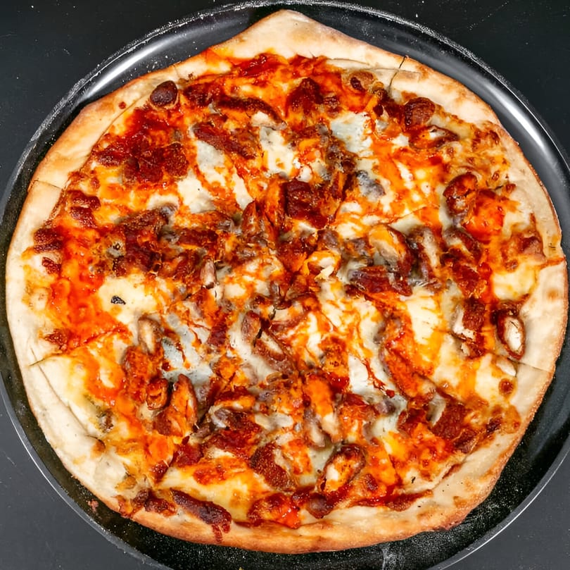 A whole Bruno's Pizza with buffalo chicken, cheese, and a drizzle of hot sauce.