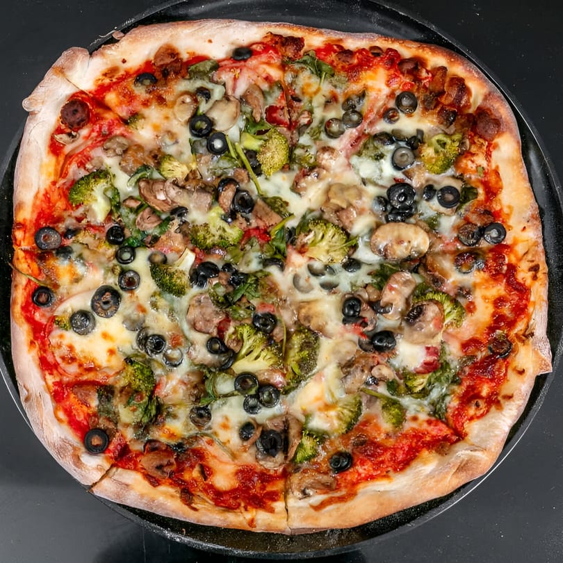 Bruno's Pizza with broccoli, mushrooms, and black olives on a dark pan.